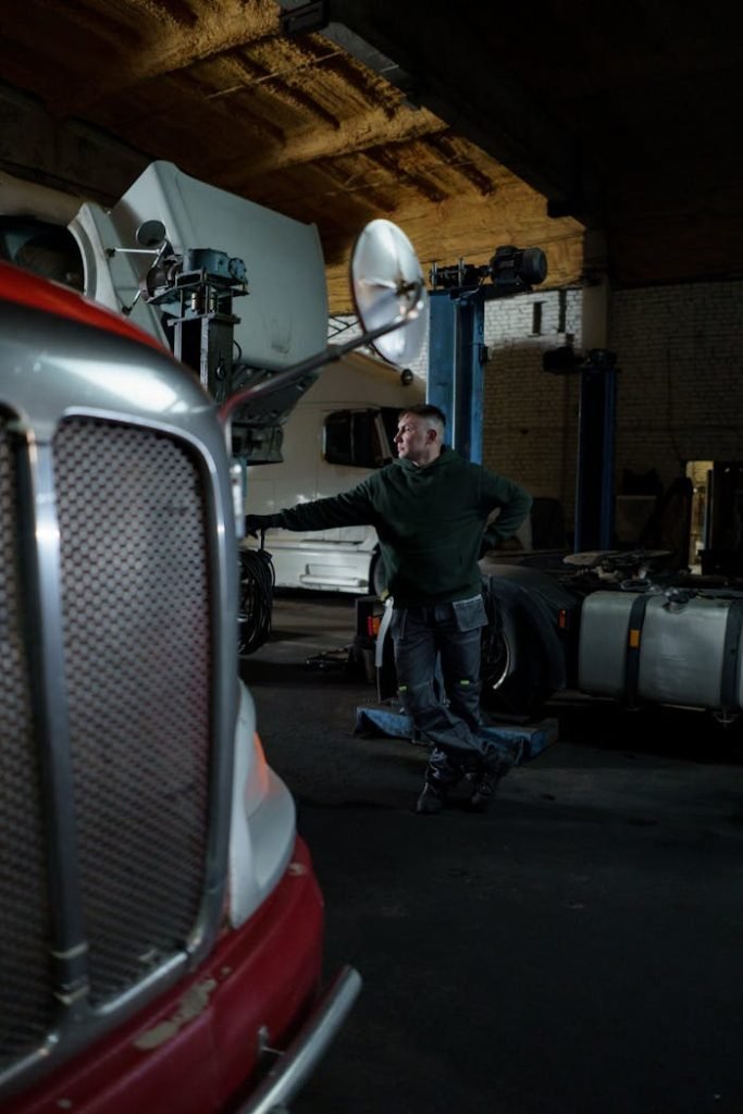 Mechanic in a dimly lit garage working on a semi-truck, capturing the essence of vehicle maintenance and repair.