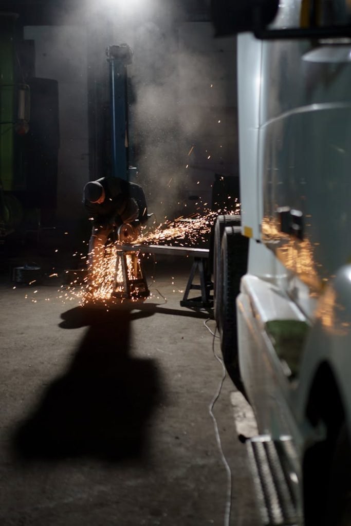 Welder sparks fly as vehicle frame repaired in an indoor garage setting.